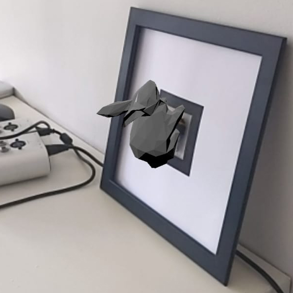 A blue square picture frame leans against a wall. Inside the frame, an augmented reality model of a rabbit is projected onto a woven marker. The weaving cannot be seen.