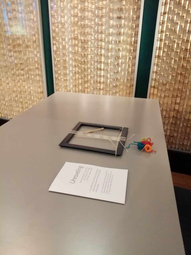A table in the Grant Museum of Zoology with an A5 paper handout for Unravelling, a warped up hand loom and a selection of colourful yarns.