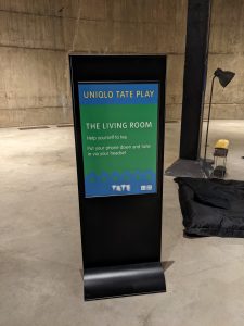 Sign inside a concrete room with the words Uniqlo Tate Play The Living Room